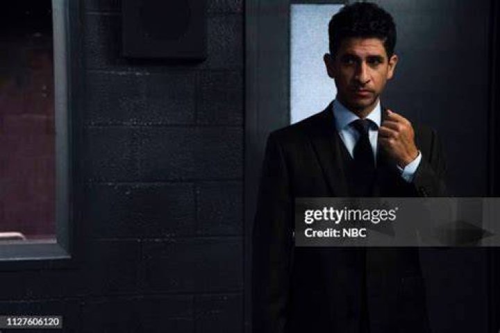 Raza Jaffrey in black formal dress posing with his wife Lara Pulver in a grey bodycon and golden jewelry.